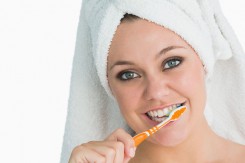 Woman with hair towel washing her teeth in the white background